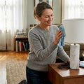 Woman dusting marble lamp in sunlit living room